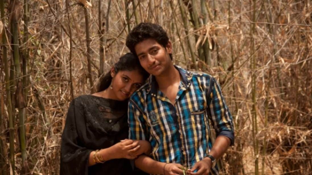 A young couple stands close together in a dry bamboo