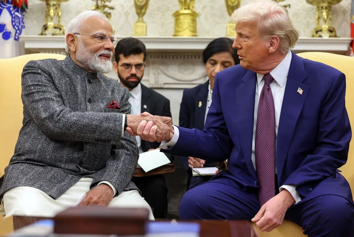Indian Prime Minister Narendra Modi and former U.S. President Donald Trump shake hands during a formal meeting in an elegant room with golden decorations in the background. Both leaders are seated, engaging in conversation, with officials taking notes behind them.
