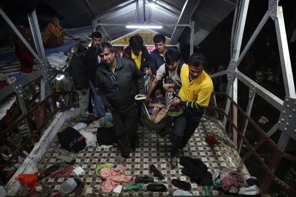 "Rescue workers carrying an injured person on a stretcher down a footbridge littered with scattered belongings, shoes, and clothes. The scene is dimly lit, with people in yellow and dark clothing assisting in the rescue effort."