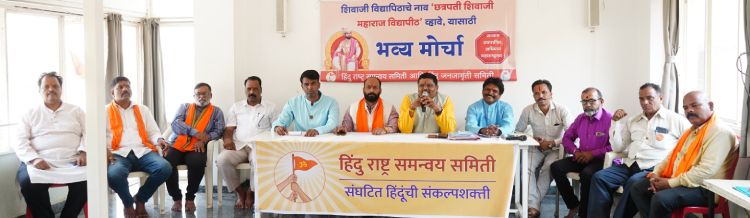 A group of men sits at a long table in a conference room, participating in a press conference or meeting. The table is covered with a banner that reads "हिंदू राष्ट्र समन्वय समिती" (Hindu Rashtra Coordination Committee) and "संघटित हिंदुंची संकल्पशक्ती" (Organized Hindus' Determination). Behind them, a large banner with Marathi text promotes an event called "भव्य मोर्चा" (Grand March) and mentions issues related to education and religious matters. Some participants wear saffron scarves, while others are dressed in formal and semi-formal attire. The setting appears to be an indoor hall with natural light entering from windows.