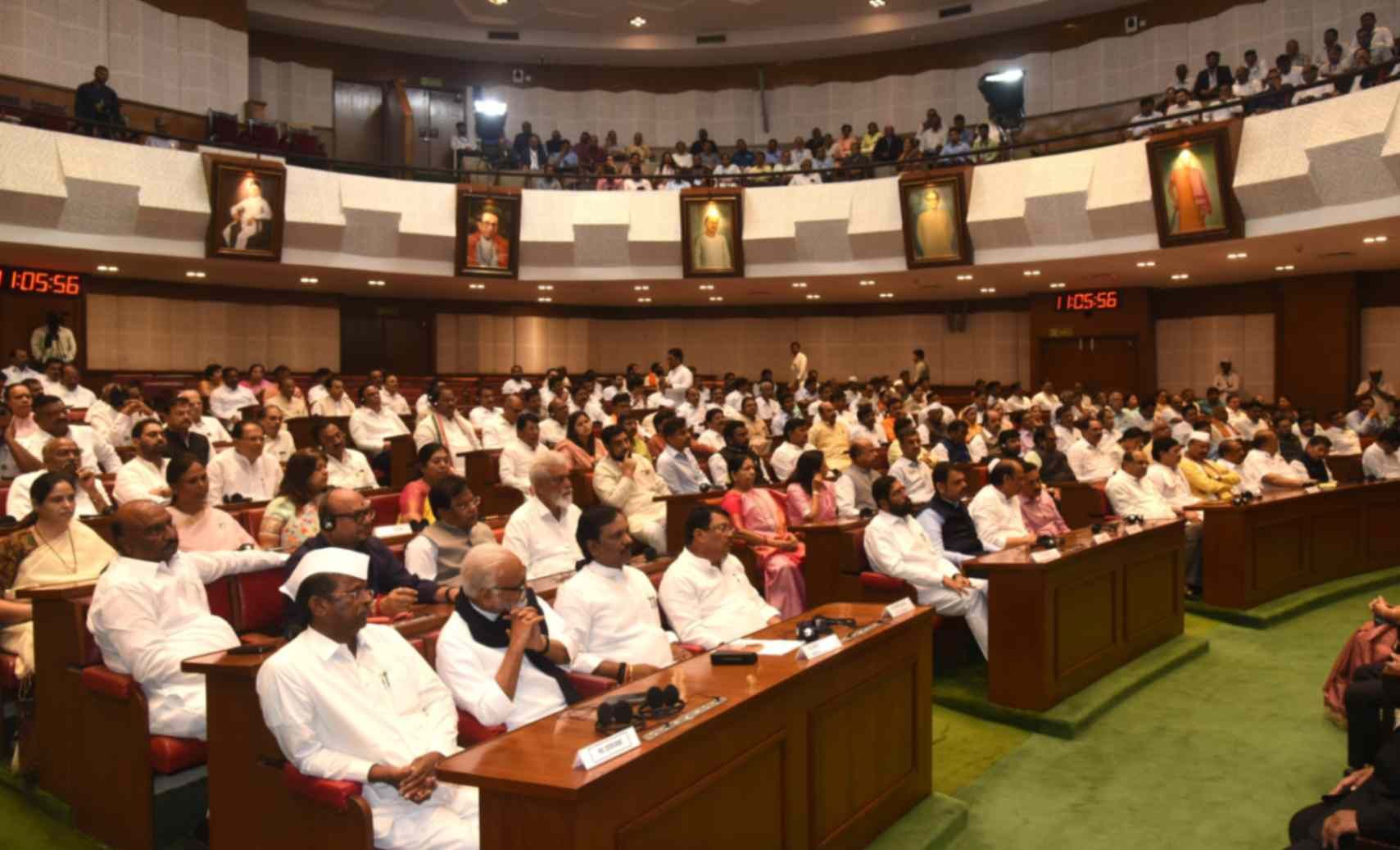 This image depicts a legislative assembly hall filled with a large number of people, including politicians, officials, and attendees. Many individuals are dressed in traditional white attire, indicating a formal political gathering. The hall is structured with seating arrangements and decorated with portraits of prominent figures on the walls. The atmosphere suggests an ongoing discussion, debate, or important legislative session.