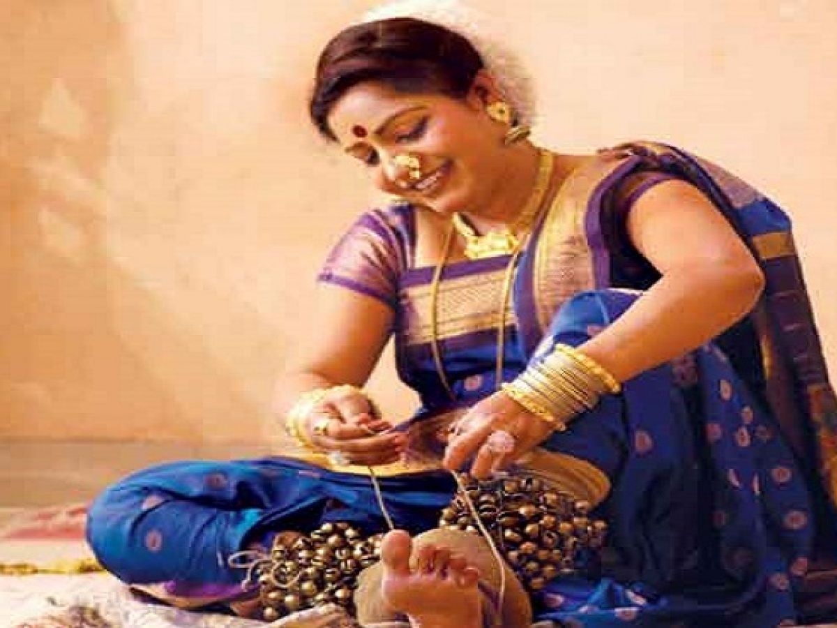 "A close-up of a dancer’s feet adorned with traditional ghungroos (ankle bells) in motion. The dancer is barefoot, and the bells create a rhythmic visual as they move on a polished floor. The background is slightly blurred, highlighting the intricate details of the ghungroos and the dancer's footwork."